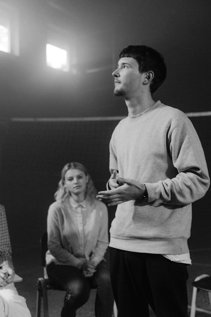 A young man speaks passionately during a group therapy session, in a monochrome setting.